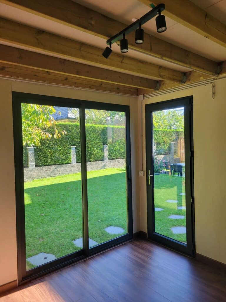 Intérieur de studio de jardin avec baies vitrées coulissantes, plafond à poutres bois et parquet stratifié