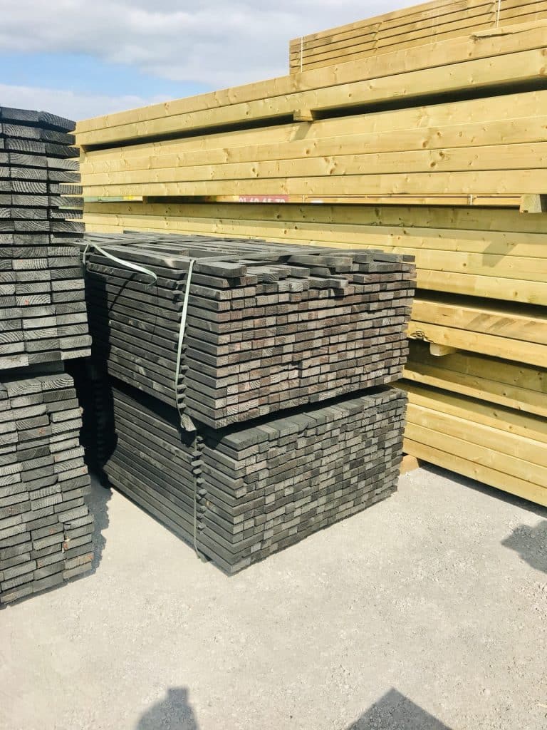 Stock de madriers pin traite autoclave et lames de terrasse grises empilees en depot exterieur