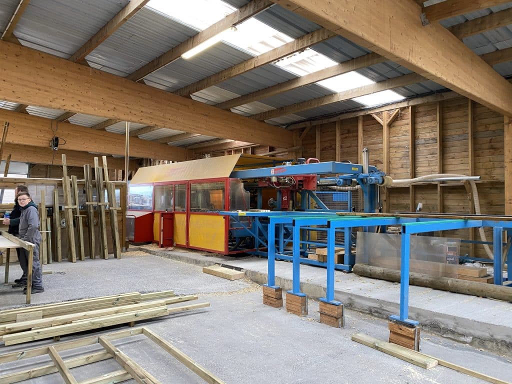 Interieur atelier scierie avec ligne de production bleue et collaboratrice de l equipe Abri Francais au travail