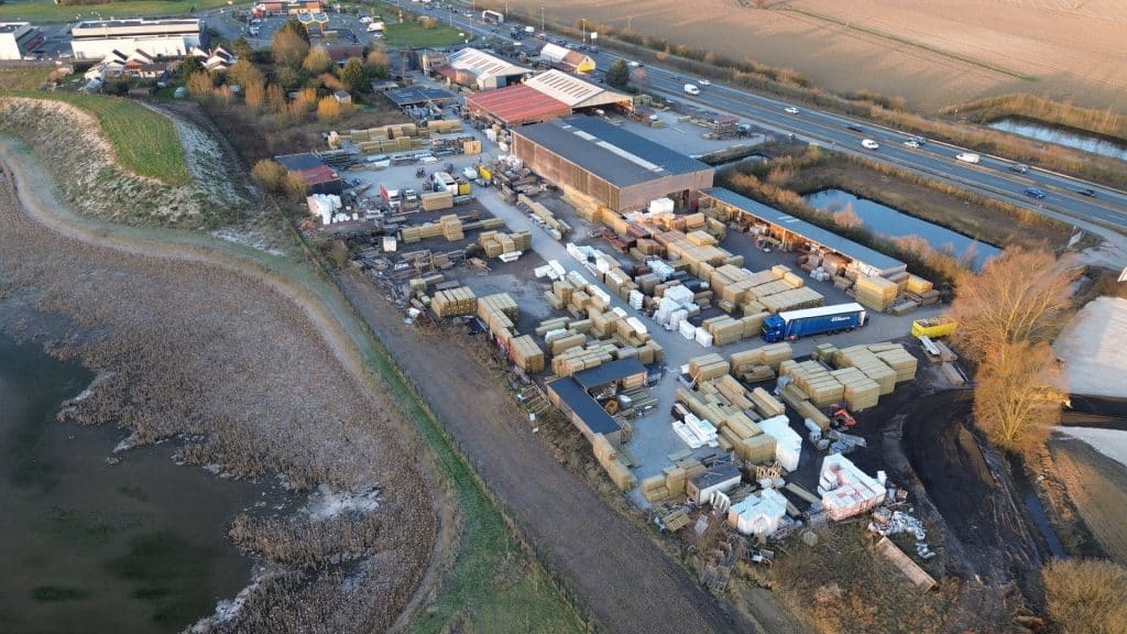 Vue aérienne du site de production avec hangars, stocks de palettes de bois et bassin en bordure d'autoroute